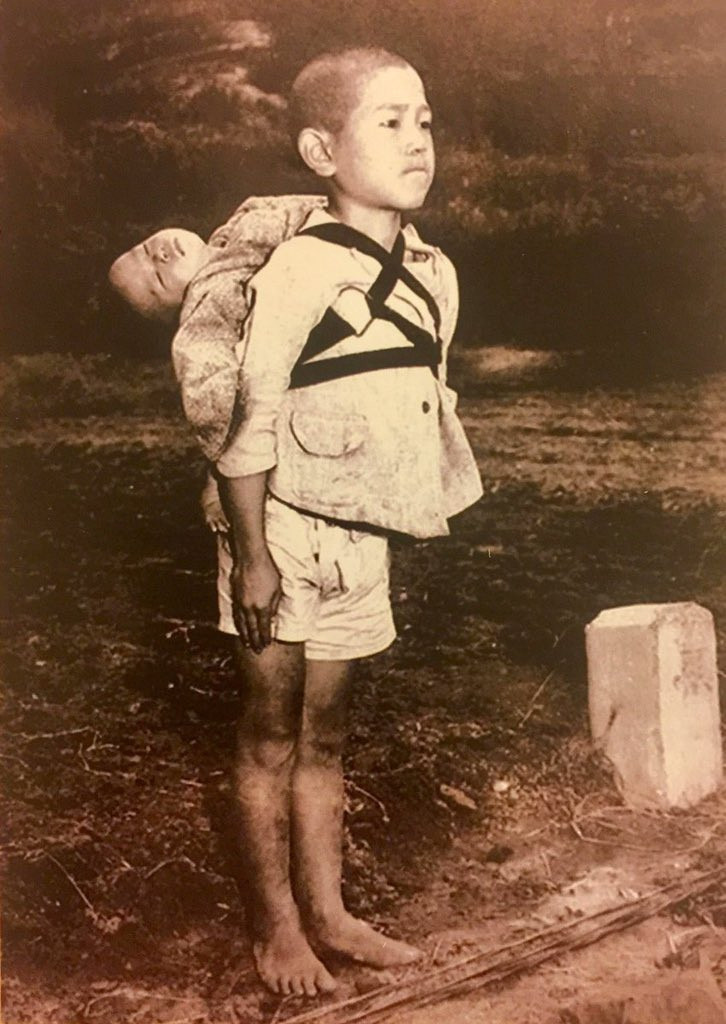 Jaapani poiss ootab krematooriumi järjekorras koos oma surnud väikevennaga, kes on talseljas. Nagasaki, 1945